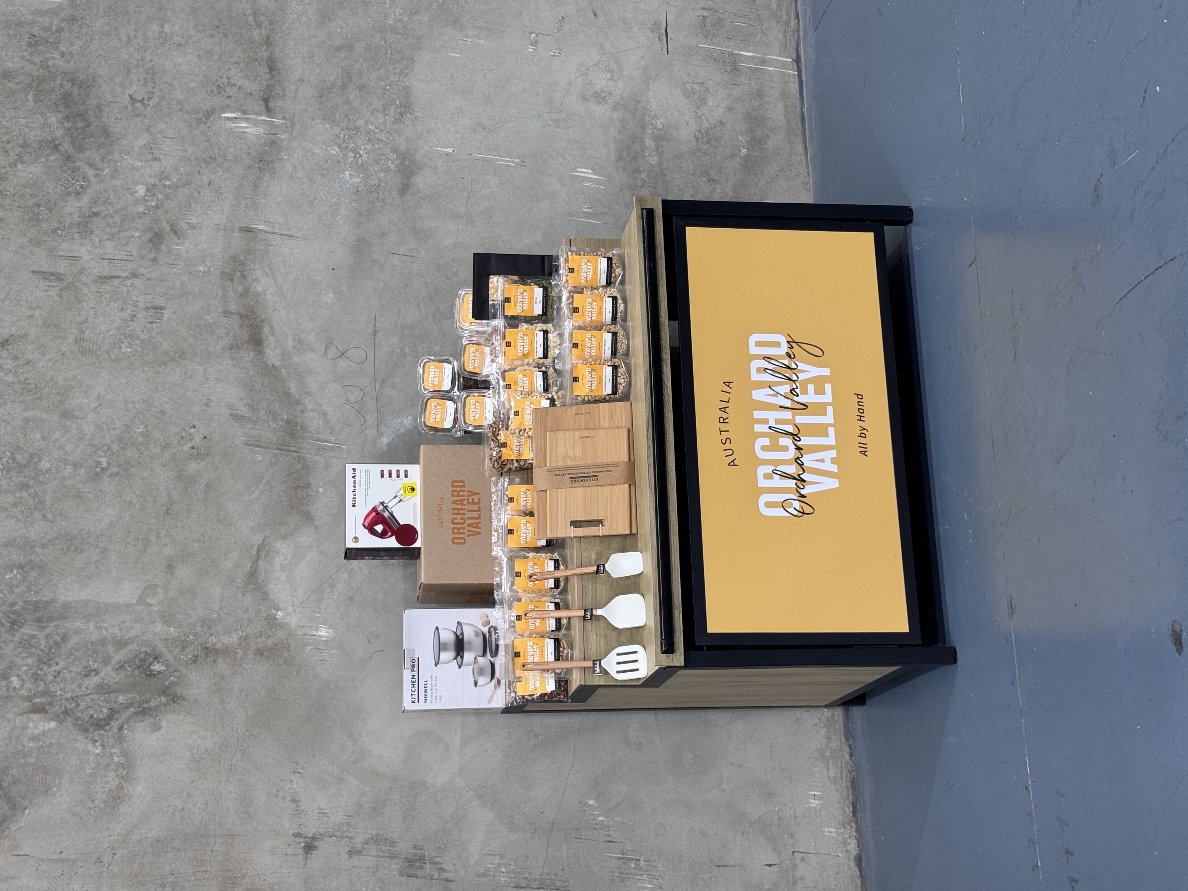 The prize bundle — KitchenAid hand mixer, bamboo chopping boards, mixing bowls, utensils and Orchard Valley product on an Orchard Valley branded display
